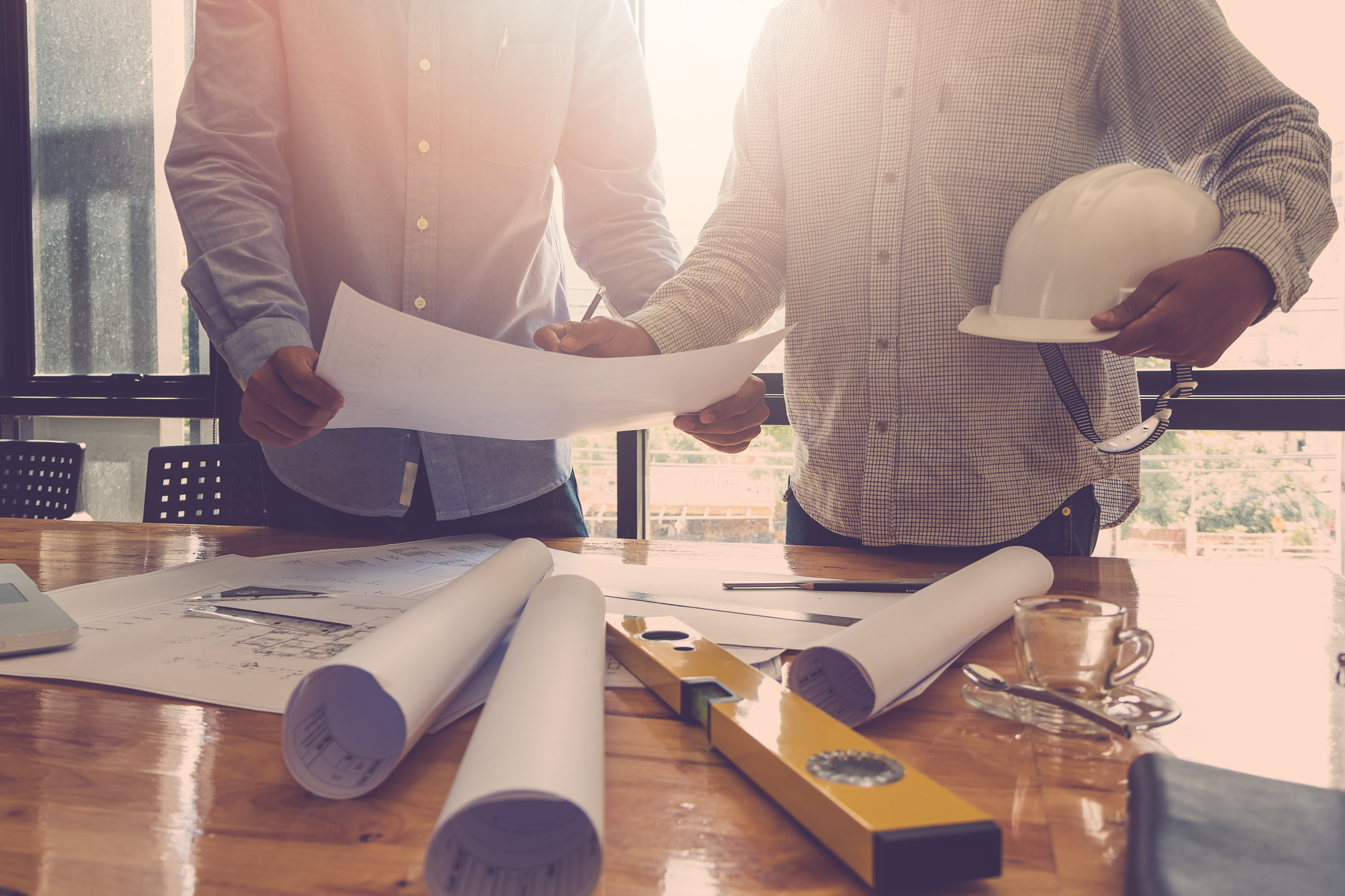 Close up of two men holding hard hats and rolled up plans