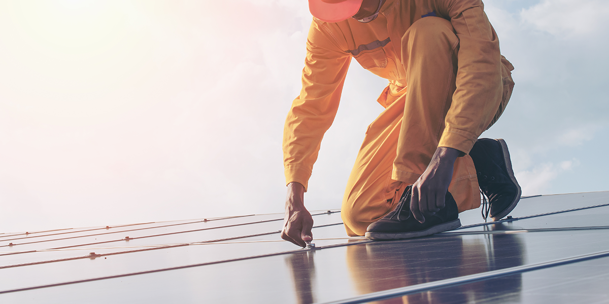A solar panel worker wearing an orange jumpsuit while fixing solar panels
