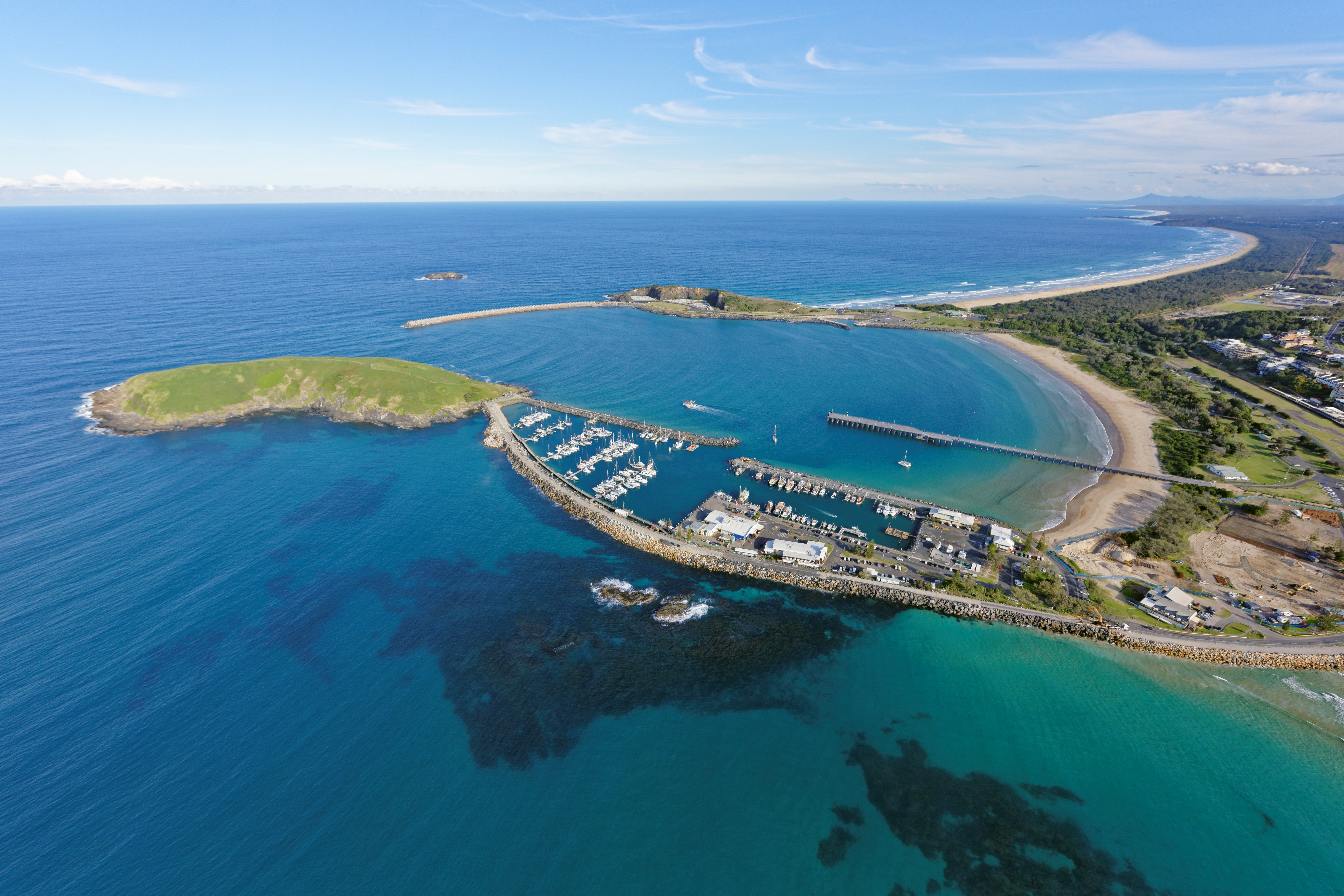 An aerial shot of the Coffs Harbour jerry and marina featuring crystal clear water, boats and land